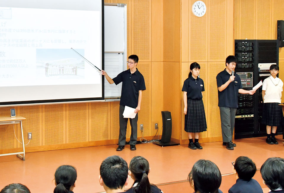 スクリーンを使って壇上で企業について発表している生徒たち